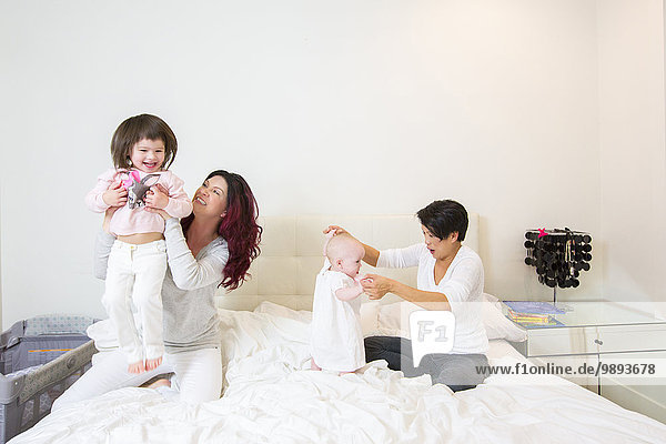 Female couple on bed having fun with baby and toddler daughters