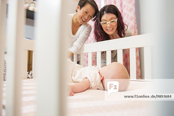 Female couple watching tired baby daughter in crib