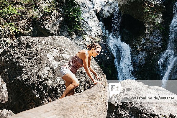 A woman climbing on rock near a waterfall