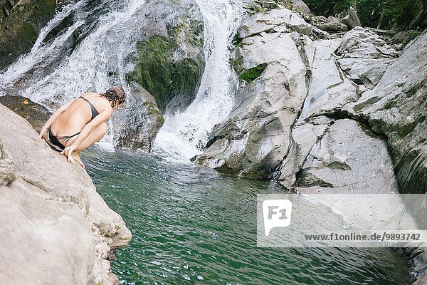 A woman contemplating jumping into a swimming hole in the woods with a waterfall