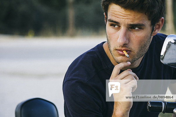 Junger Mann  der auf seinem Motorrad raucht