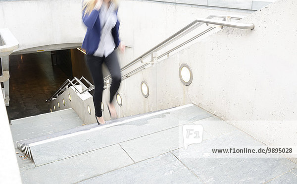 Telefonierende Geschäftsfrau,  die eine Treppe hinaufläuft.