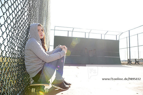 Traurige Frau sitzt auf ihrem Skateboard auf einem Sportplatz.