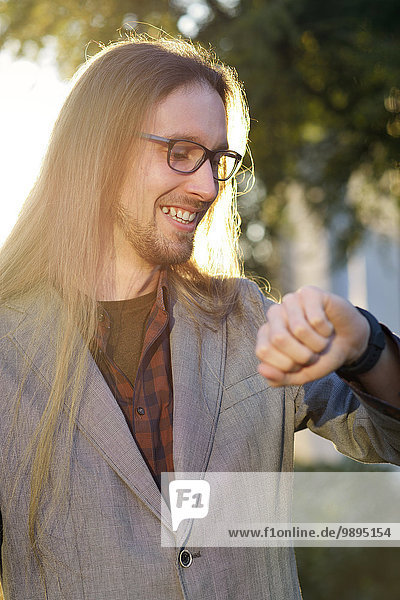 Porträt eines lächelnden langhaarigen Hipsters mit Blick auf seine smartwatch