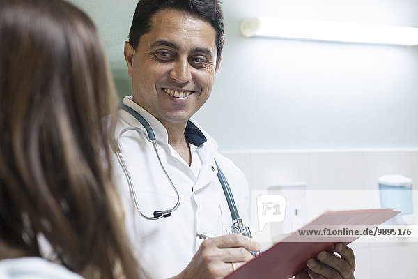 Lächelnder Arzt  der sich Notizen macht  während er dem Patienten zuhört.