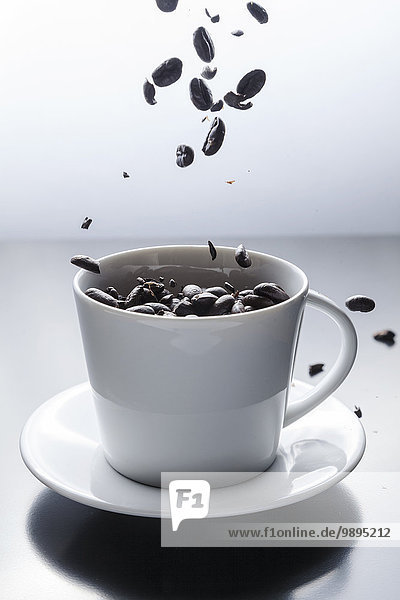 Kaffeebohnen,  die in eine weiße Kaffeetasse fallen