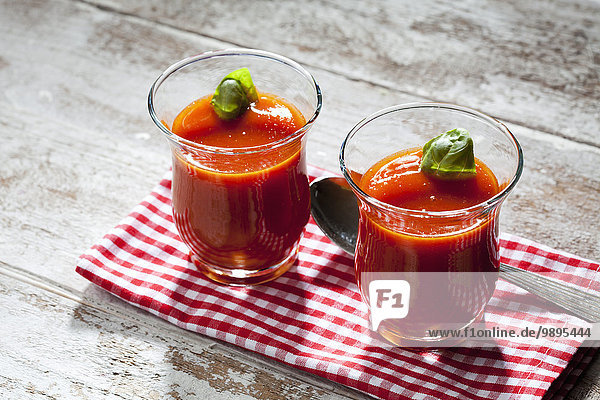 Zwei Gläser Tomatensuppe mit Basilikumblatt garniert
