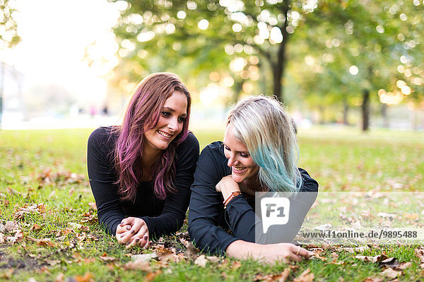 Two female friends with coloured hair lying on a meadow