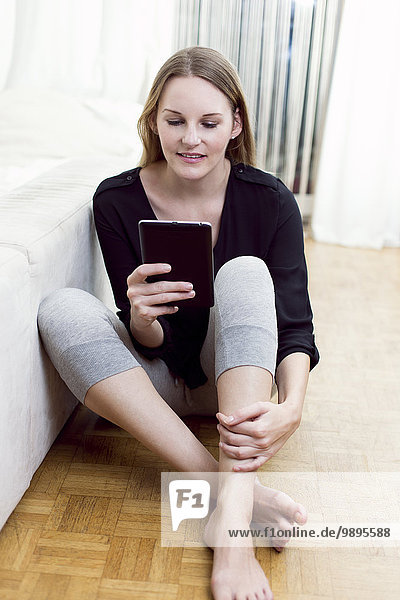 Porträt einer auf dem Boden sitzenden Frau mit Mini-Tablette