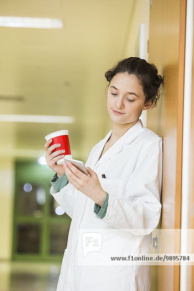 Junger Arzt mit Handy und Kaffeetasse auf dem Krankenhausboden