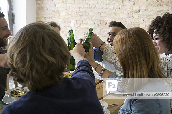 Happy friends eating together clinking beer bottles