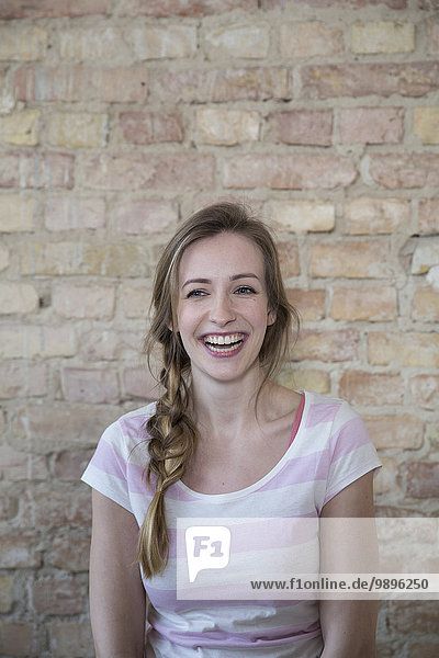 Portrait of laughing young woman in front of brick wall