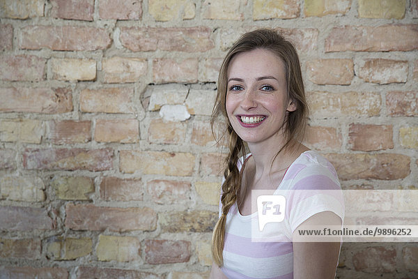 Portrait of smiling young woman in front of brick wall