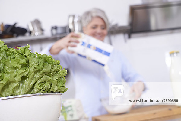 Salat und reife Frau in der Küche gießen Mehl in Schüssel
