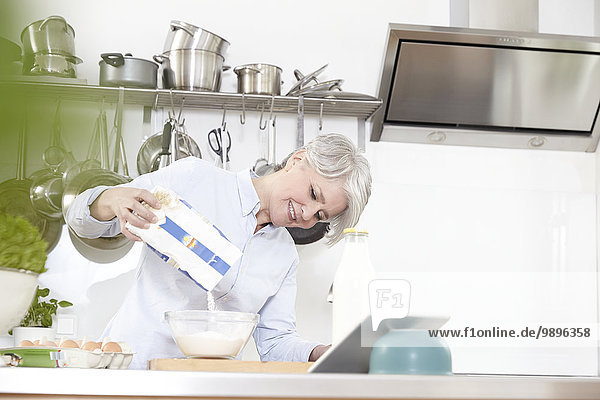 Reife Frau in der Küche gießt Mehl in die Schüssel