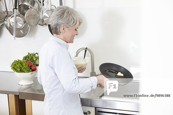 Reife Frau in der Küche bei der Zubereitung von Pfannkuchen