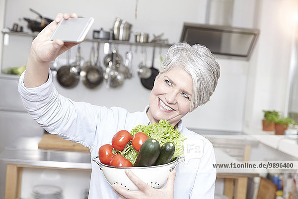 Reife Frau hält Sieb mit Gemüse unter Selbstbedienung