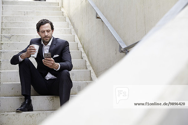 Businessman with coffee to go using smartphone in a modern building