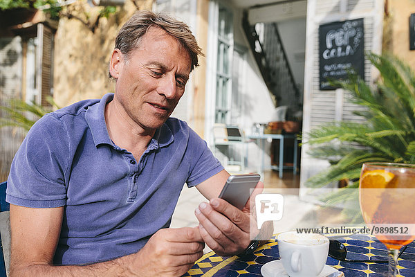 Spanien  Mallorca  Arta  Porträt eines Mannes im Hof eines Cafés mit Smartphone