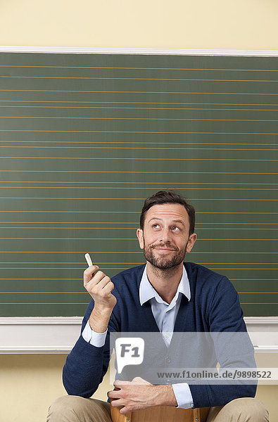 Lächelnder Lehrer im Klassenzimmer an der Tafel schaut nach oben Lächelnder Lehrer im Klassenzimmer an der Tafel schaut nach oben