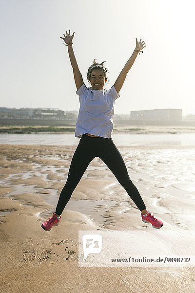 Spanien  Gijon  glückliche junge Frau beim Springen am Strand
