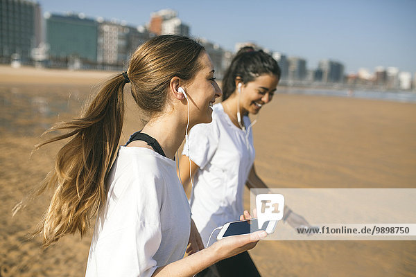 Spanien  Gijon  zwei sportliche junge Frauen mit Ohrstöpseln am Strand