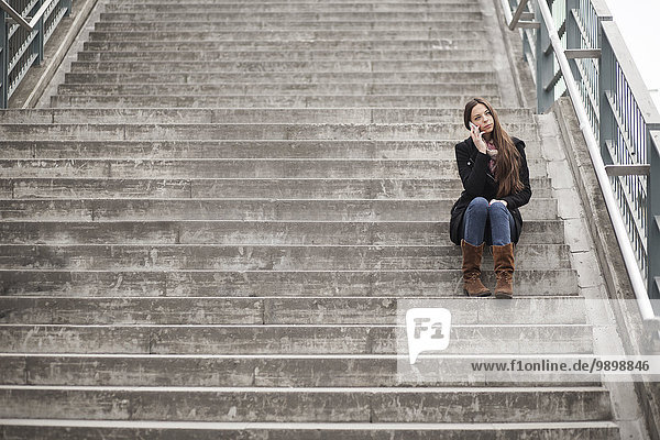 Junge Frau sitzt auf der Treppe und telefoniert mit dem Smartphone.