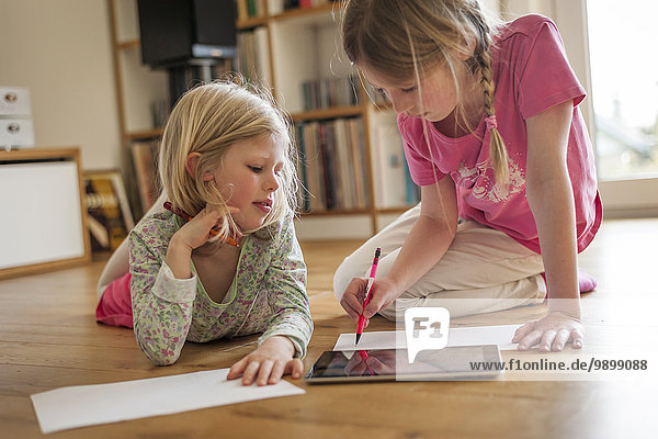 Two sisters with digital tablet and sheets of paper on floor