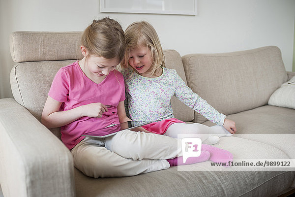 Zwei Schwestern mit digitalem Tablett auf der Couch