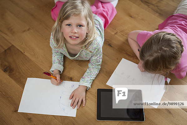 Zwei Schwestern mit digitalem Tablett und Papierbögen auf dem Boden