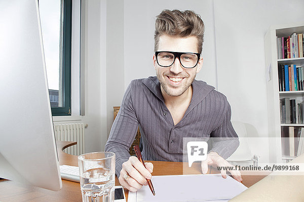 Porträt eines lächelnden jungen Mannes am Schreibtisch im Büro