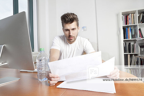 Junger Mann beobachtet Dokumente am Schreibtisch in einem Büro