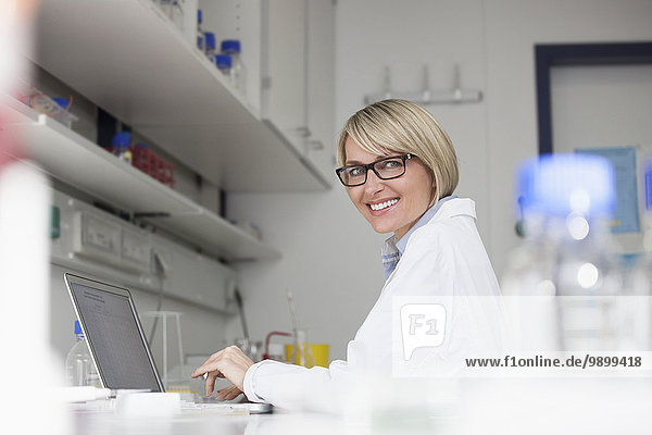 Smiling scientist using laptop in laboratory