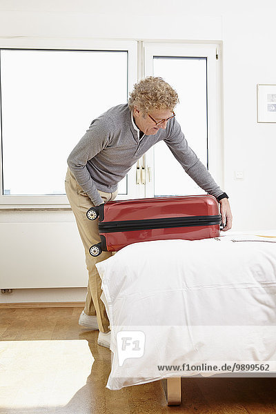 Senior man packing suitcase in bedroom