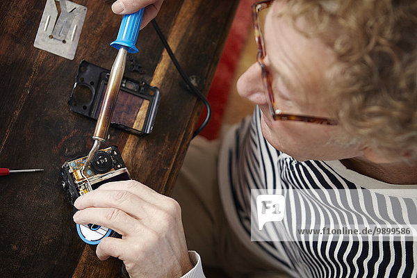 Senior man soldering broken camera