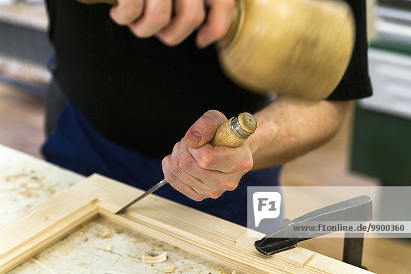 Rahmenbauer bei der Arbeit an einem Holzrahmen mit Hammer und Meißel