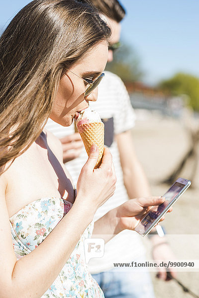 Young couple with ice cream cone and smartphone outdoors in summer