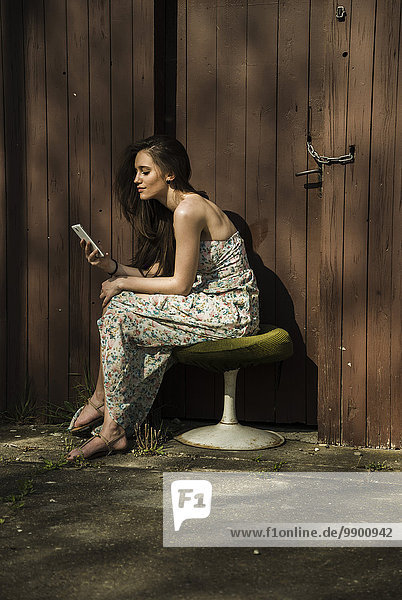 Junge Frau sitzend auf altem Hocker mit Handy