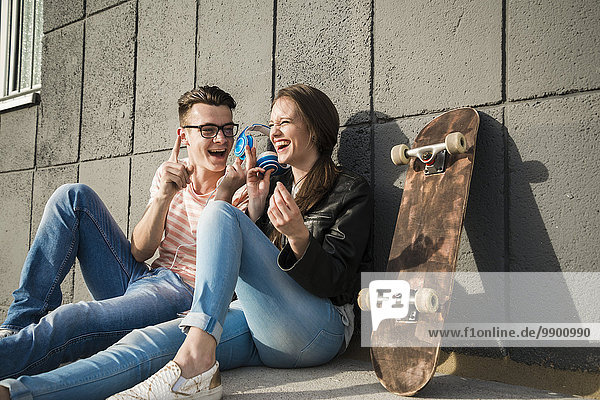 Glückliches junges Paar auf dem Boden sitzend mit Kopfhörer und Skateboard