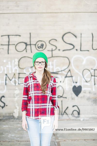 Junge Frau mit kariertem Hemd und grünem Wollhut an der Graffiti-Wand