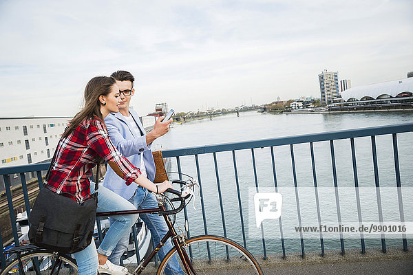 Deutschland Mannheim junger Mann und Frau mit Fahrrad und Handy auf Brücke