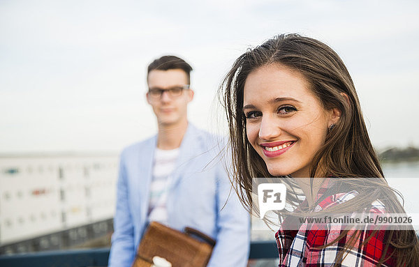 Lächelnde junge Frau mit Mann im Hintergrund