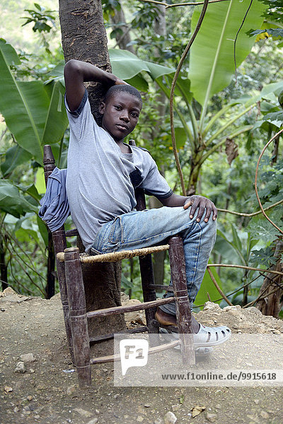 Teenager boy on a rickety chair  Riviere Froide  Ouest Department  Haiti  North America