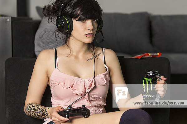Young woman gaming in the living room  with a Playstation controller  headphones and a Monster energy drink can