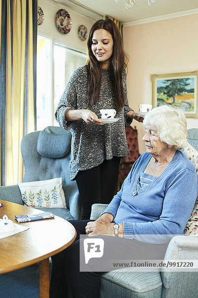 Junge Frau hält Kaffeetassen  während sie zu Hause bei ihrer Großmutter steht.