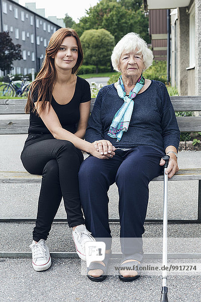 Porträt einer lächelnden Frau  die mit ihrer Enkelin auf einer Bank im Freien sitzt.