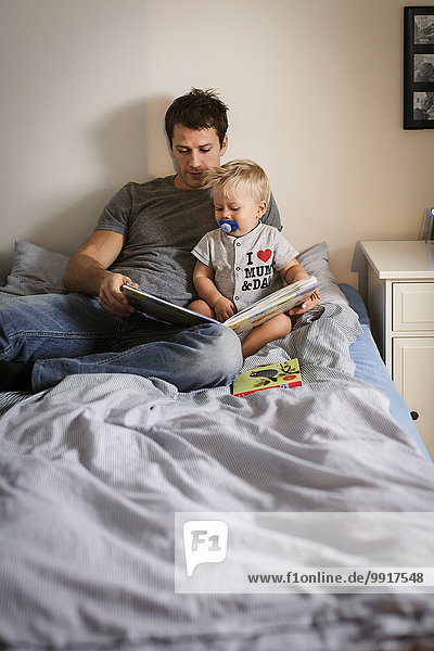 Man reading book with baby boy in bedroom