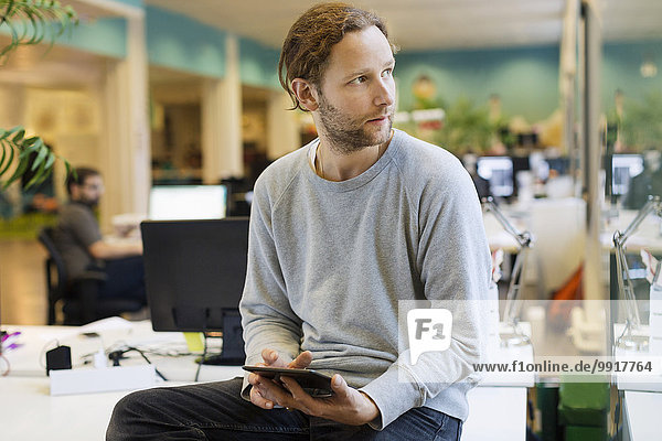 Businessman looking away while holding digital tablet on desk in creative office