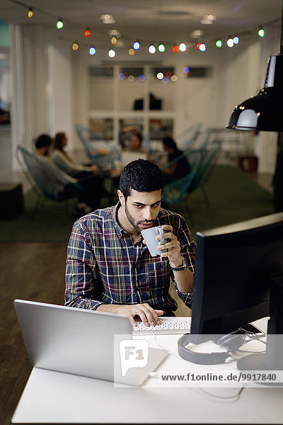 Geschäftsmann beim Kaffeetrinken während der späten Arbeit im Kreativbüro
