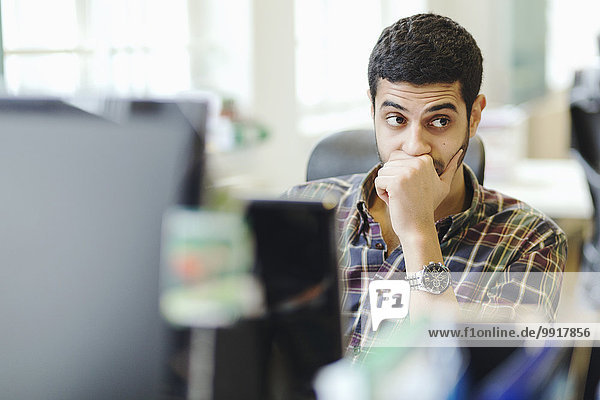 Businessman looking away while sitting at desk in creative office